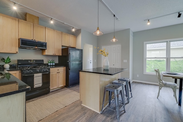 kitchen featuring black appliances, a center island, light brown cabinetry, and wood-type flooring