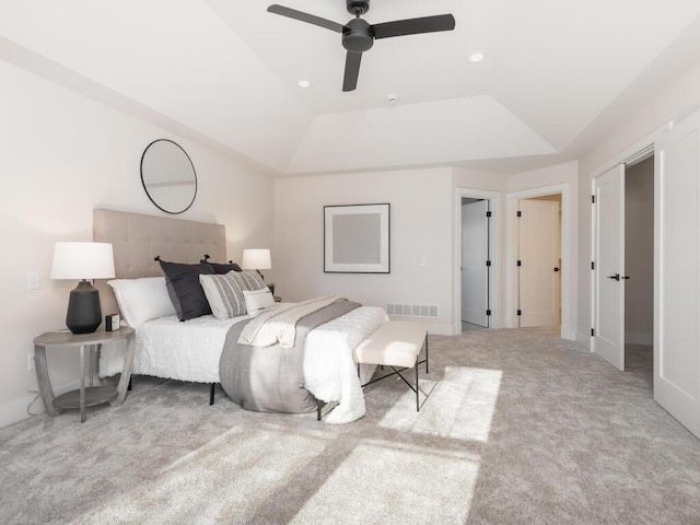 bedroom with light colored carpet, a raised ceiling, and ceiling fan