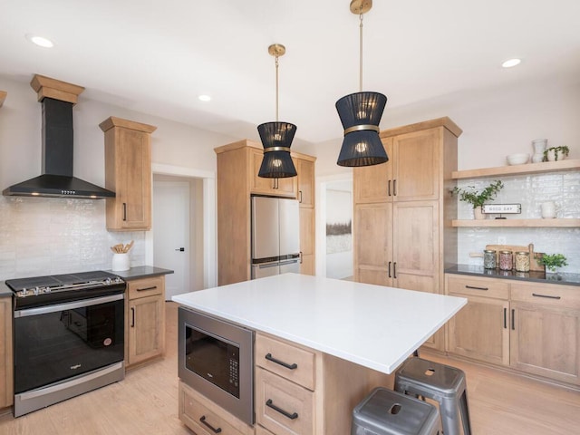 kitchen featuring appliances with stainless steel finishes, pendant lighting, tasteful backsplash, wall chimney range hood, and light hardwood / wood-style flooring