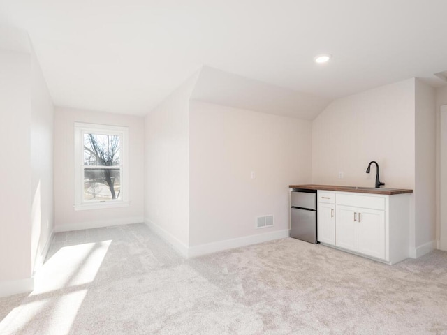 bar featuring sink, white cabinetry, vaulted ceiling, light carpet, and stainless steel fridge