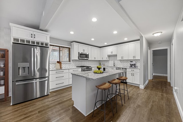 kitchen with a kitchen island, dark hardwood / wood-style floors, white cabinets, a kitchen bar, and stainless steel appliances