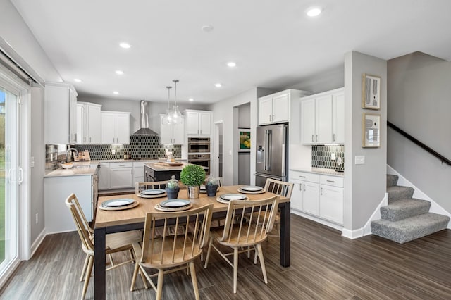 kitchen with appliances with stainless steel finishes, white cabinetry, wall chimney range hood, decorative light fixtures, and dark wood-type flooring