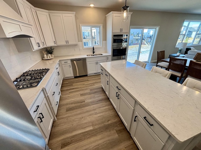 kitchen with hardwood / wood-style floors, stainless steel appliances, tasteful backsplash, white cabinets, and decorative light fixtures