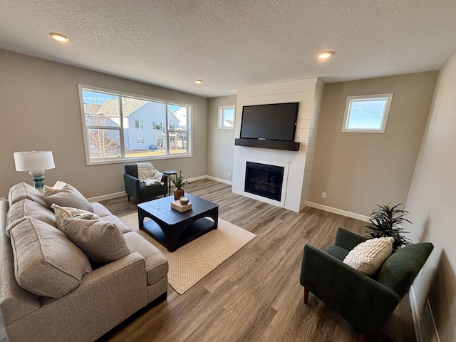 living room featuring hardwood / wood-style flooring, a large fireplace, and a textured ceiling