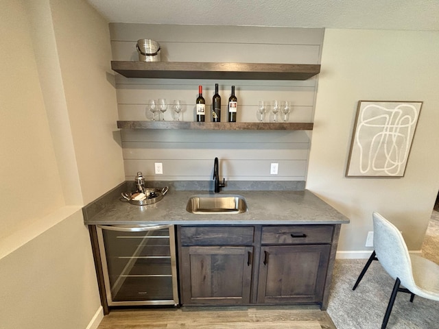 bar featuring dark brown cabinets, sink, beverage cooler, and light hardwood / wood-style flooring