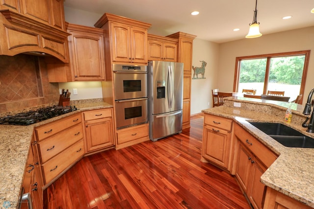 kitchen featuring stainless steel appliances, hanging light fixtures, sink, and light stone counters