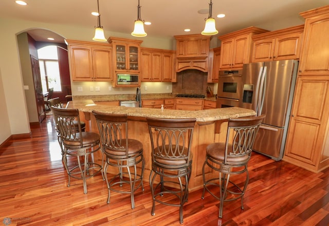 kitchen featuring sink, appliances with stainless steel finishes, light stone countertops, a center island with sink, and decorative light fixtures