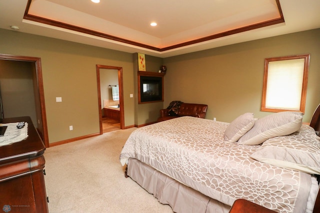 bedroom featuring light colored carpet, ensuite bathroom, and a tray ceiling