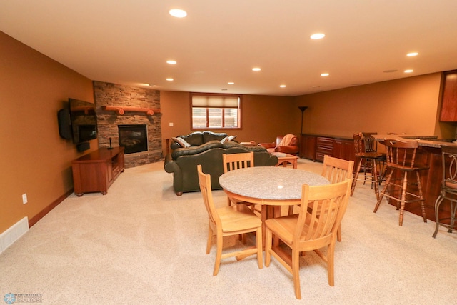 dining room featuring a stone fireplace, light carpet, and indoor bar