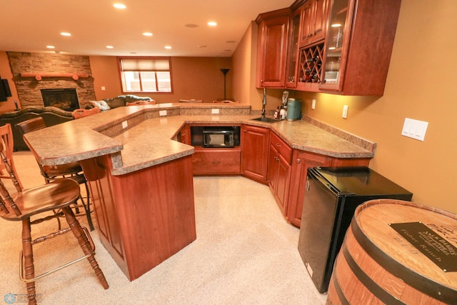 kitchen with a stone fireplace, a breakfast bar, sink, kitchen peninsula, and light stone countertops