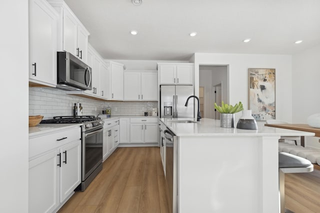 kitchen featuring appliances with stainless steel finishes, white cabinetry, tasteful backsplash, a center island with sink, and a breakfast bar area