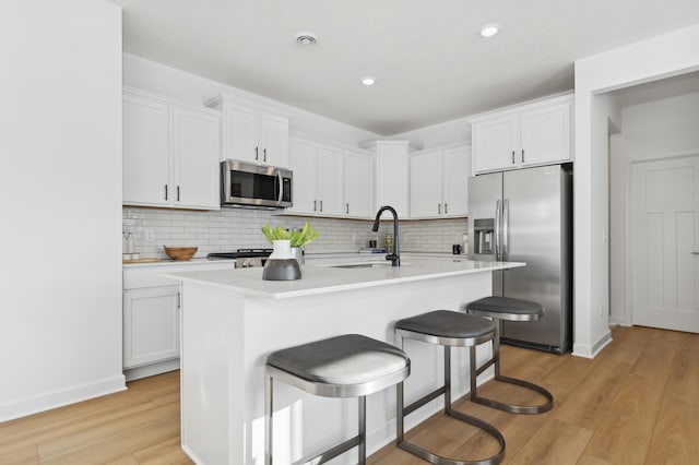 kitchen with a kitchen breakfast bar, a kitchen island with sink, white cabinetry, and stainless steel appliances