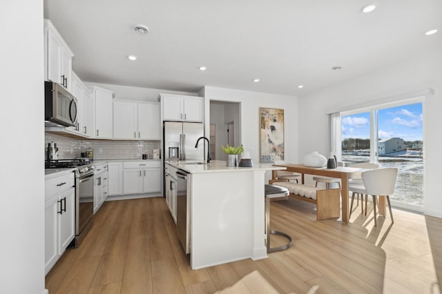 kitchen with appliances with stainless steel finishes, white cabinetry, tasteful backsplash, an island with sink, and light wood-type flooring