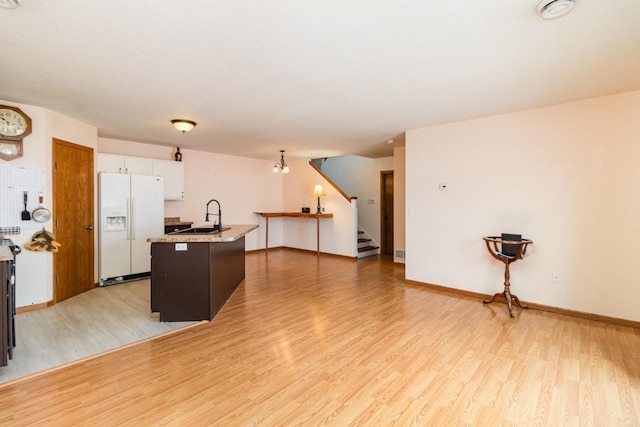 kitchen with sink, light hardwood / wood-style flooring, white cabinetry, a kitchen island with sink, and white fridge with ice dispenser