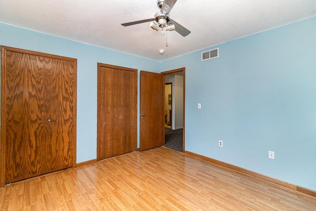 unfurnished bedroom with two closets, light hardwood / wood-style floors, ceiling fan, and a textured ceiling