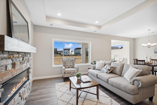 living room with a tray ceiling, a stone fireplace, an inviting chandelier, and hardwood / wood-style flooring