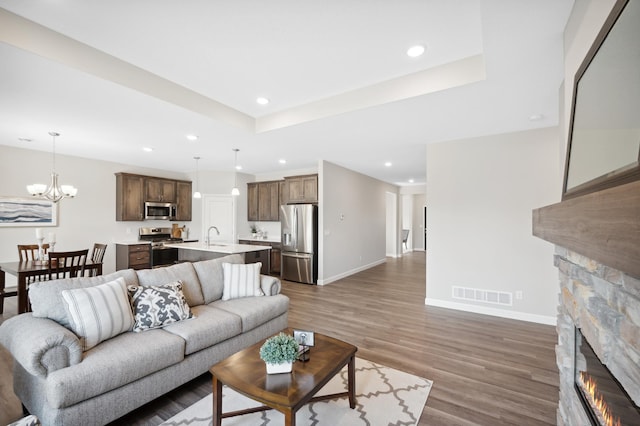 living room with sink, dark wood-type flooring, a tray ceiling, a fireplace, and a chandelier