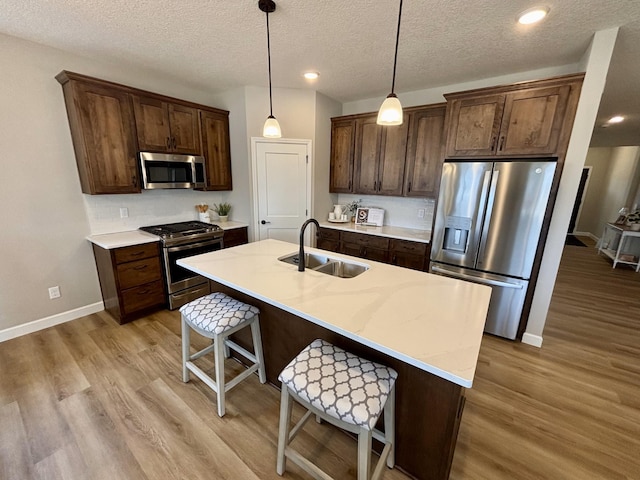 kitchen with a breakfast bar, a sink, light countertops, appliances with stainless steel finishes, and light wood-type flooring