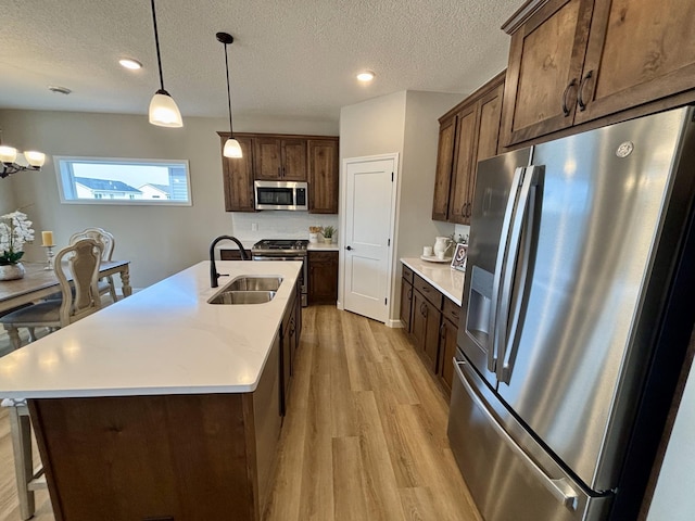 kitchen with a sink, hanging light fixtures, light countertops, stainless steel appliances, and light wood-type flooring