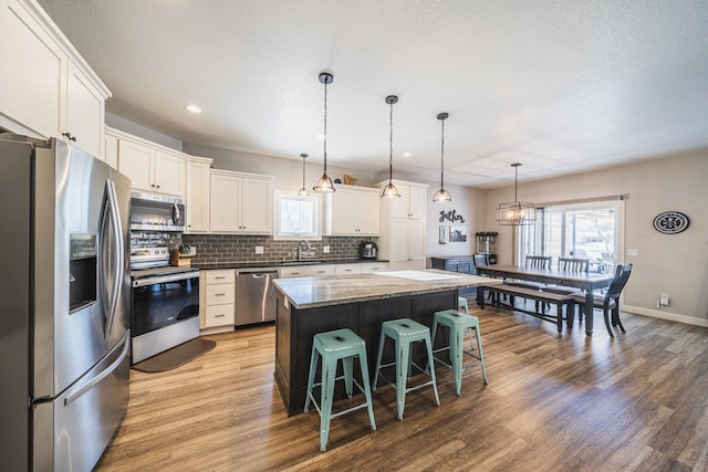 kitchen featuring sink, appliances with stainless steel finishes, hanging light fixtures, white cabinets, and a kitchen island