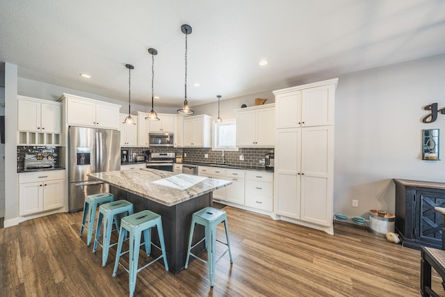 kitchen featuring a kitchen island, decorative light fixtures, white cabinetry, a kitchen bar, and stainless steel appliances