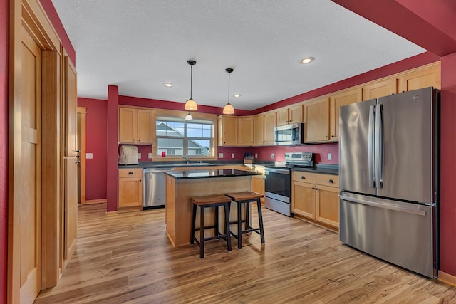 kitchen with a kitchen island, appliances with stainless steel finishes, pendant lighting, and light hardwood / wood-style flooring