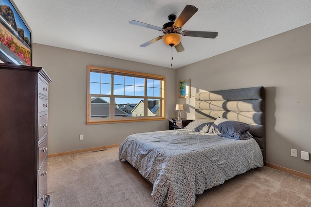 bedroom with a textured ceiling, light colored carpet, and ceiling fan