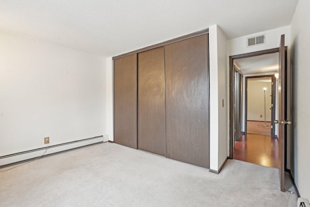 unfurnished bedroom with light carpet, a textured ceiling, baseboard heating, and a closet