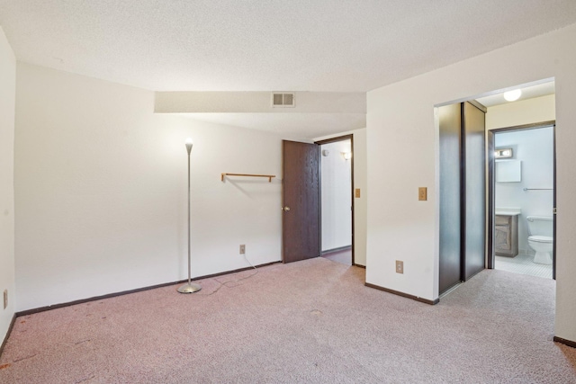 unfurnished bedroom with light colored carpet, ensuite bathroom, and a textured ceiling