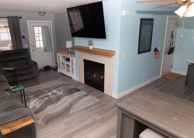 living room featuring hardwood / wood-style flooring, ceiling fan, a fireplace, and a textured ceiling