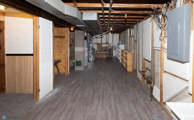 basement featuring dark wood-type flooring, wooden walls, electric panel, and gas water heater