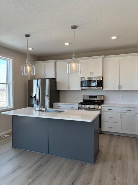 kitchen with a kitchen island with sink, a sink, light countertops, appliances with stainless steel finishes, and light wood-type flooring