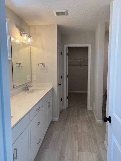 full bath featuring a walk in closet, visible vents, vanity, and baseboards
