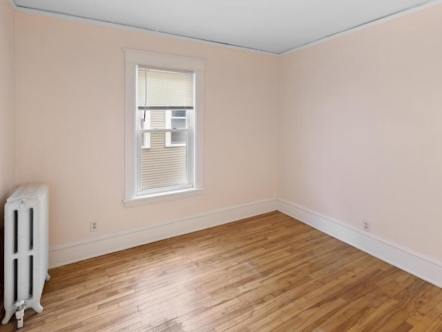 empty room with crown molding, radiator, and light hardwood / wood-style flooring