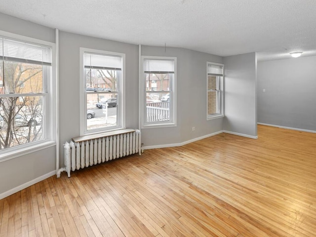 unfurnished room with light wood-type flooring, radiator heating unit, and a textured ceiling