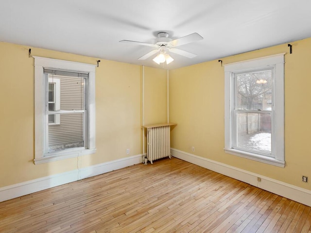 unfurnished room with radiator, plenty of natural light, ceiling fan, and light wood-type flooring