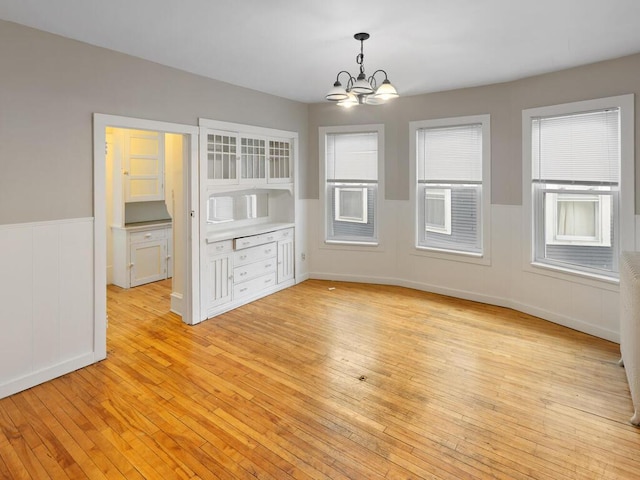 unfurnished dining area featuring an inviting chandelier, plenty of natural light, and light wood-type flooring