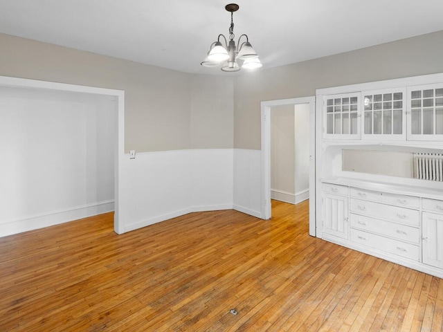 unfurnished dining area with radiator, light hardwood / wood-style floors, and a chandelier