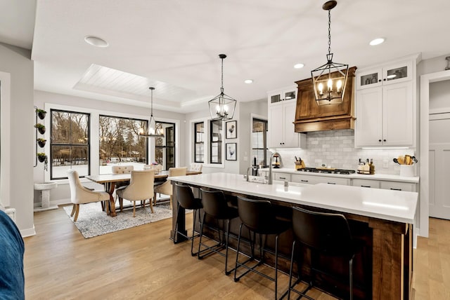 kitchen featuring white cabinetry, gas stovetop, hanging light fixtures, and an island with sink