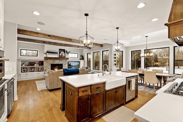 kitchen featuring sink, hanging light fixtures, stainless steel dishwasher, an island with sink, and a fireplace