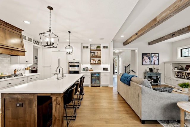 kitchen featuring appliances with stainless steel finishes, beverage cooler, a kitchen breakfast bar, a center island with sink, and beam ceiling