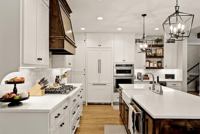 kitchen featuring sink, white cabinetry, decorative light fixtures, appliances with stainless steel finishes, and a kitchen island with sink