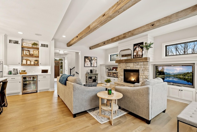 living room with bar area, light hardwood / wood-style flooring, beverage cooler, beamed ceiling, and a fireplace