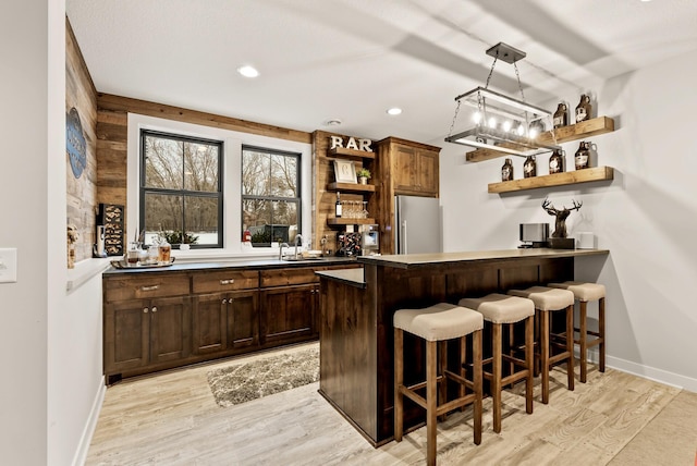 bar featuring hanging light fixtures, sink, stainless steel refrigerator, and light hardwood / wood-style floors