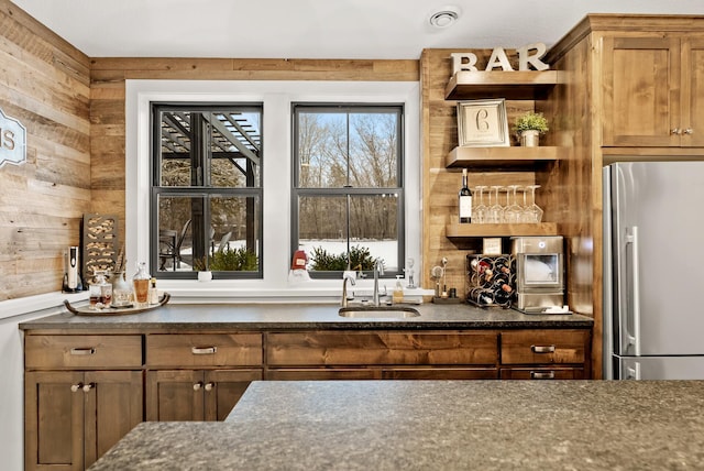 bar featuring sink, wooden walls, and stainless steel refrigerator