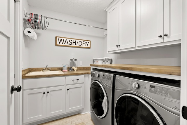 laundry area featuring sink, light hardwood / wood-style flooring, cabinets, a textured ceiling, and separate washer and dryer