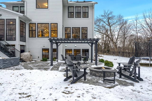 snow covered back of property featuring a trampoline, a pergola, and a fire pit