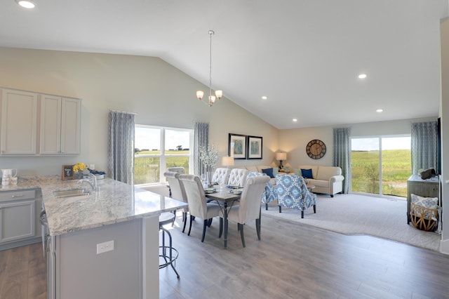 dining room featuring high vaulted ceiling, sink, a chandelier, and light wood-type flooring