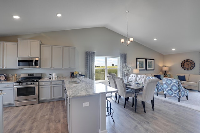 kitchen featuring stainless steel appliances, light hardwood / wood-style floors, sink, hanging light fixtures, and a breakfast bar area