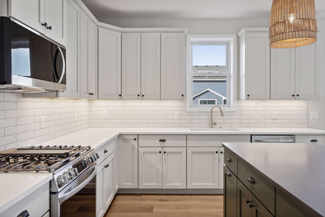 kitchen with tasteful backsplash, white cabinetry, sink, stainless steel appliances, and light wood-type flooring